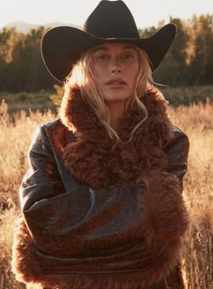Woman in a cowboy hat and fur-lined coat outdoors during golden hour