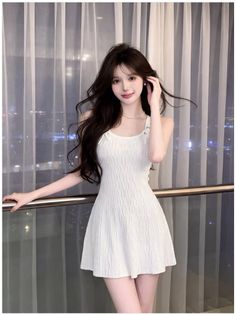 Woman in a white dress and pearl necklace indoors at night with a cityscape view