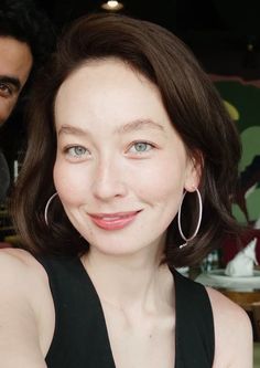 Woman with short brown hair and blue eyes smiling, wearing hoop earrings