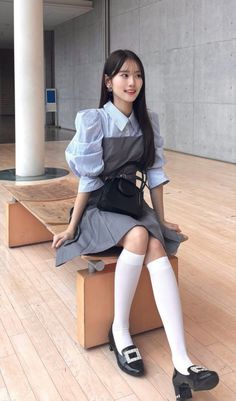 Woman with long hair wearing a striped shirt and pinafore dress, sitting indoors
