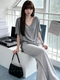 Woman with long hair wearing a gray t-shirt and wide leg pants indoors