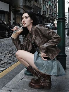 Woman in a leather jacket and denim skirt crouching on a cobblestone street