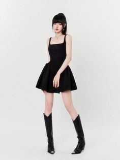 Woman in a black dress and knee-high boots posing against a white background