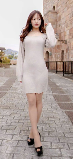 Woman in a light-colored knit dress and high heels on a stone path outdoors