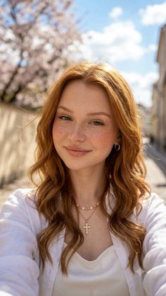Woman with red hair and freckles wearing a white shirt and jewelry outdoors