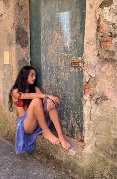 Woman with long dark hair sitting barefoot against an old wooden door