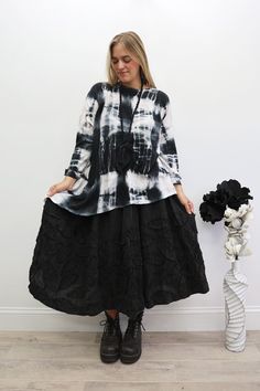 Woman in a tie-dye shirt and black skirt with combat boots indoors
