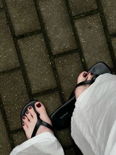 Feet in black flip flops with red nail polish on a paved ground