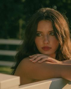 Woman with long brown hair and green eyes leaning on a white fence