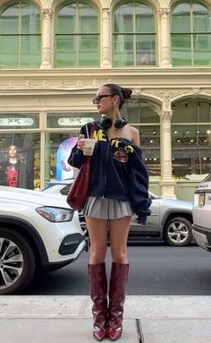 Woman in a pleated skirt and hoodie with high boots on a city street