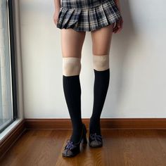 Person wearing a plaid pleated skirt, knee high socks, and brown shoes indoors