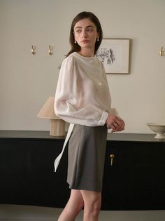 Woman in a white blouse and mini skirt with pearl earrings indoors