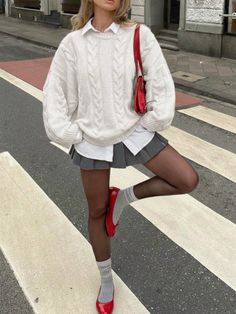 Person in a white sweater and grey mini skirt posing on a crosswalk