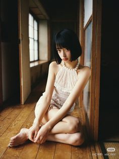 Woman with short black hair and a pearl necklace sitting on a wooden floor