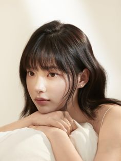 Woman with black hair and bangs resting her head on a white pillow