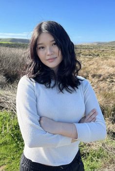 Woman with black wavy hair and freckles in a white long sleeve shirt outdoors