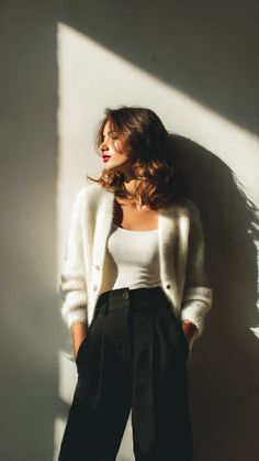 Woman in a white cardigan and black pants with dramatic lighting indoors