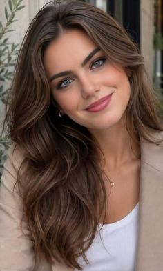 Woman with long brown hair and blue eyes wearing a beige blazer and white top