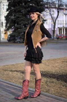 Woman in a cowboy hat, fringe vest, and black dress with cowboy boots outdoors