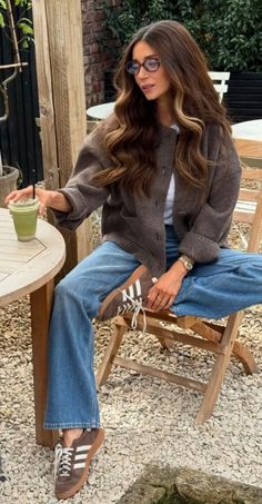 Woman with long hair and glasses sitting outdoors with a drink