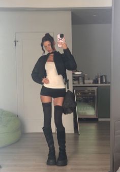 Woman in a cropped jacket, mini skirt, and thigh-high socks taking a mirror selfie