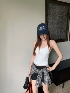 Woman in a baseball cap, white camisole, and plaid shirt tied around her waist