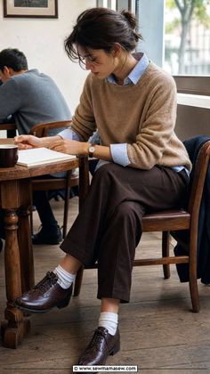 Woman in a brown sweater and blue shirt sitting at a wooden table indoors