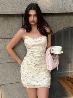 Woman in a floral dress holding a pink bag and a teacup outdoors