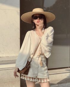 Woman in a straw hat and sunglasses wearing a long sleeve top and tassel shorts