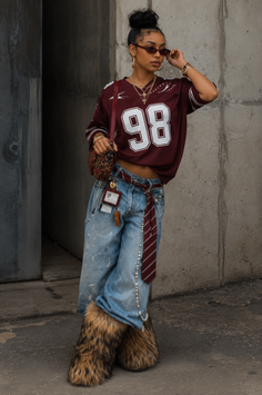 Woman in a maroon jersey, baggy jeans, and furry boots posing outdoors
