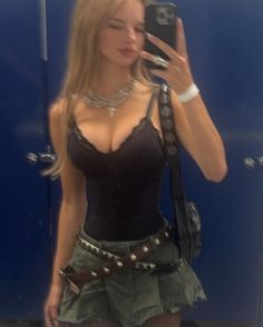 Woman in a black camisole and pleated skirt taking a mirror selfie