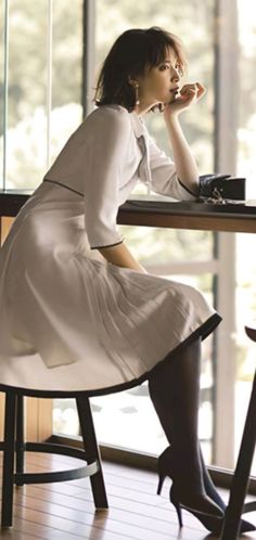 Woman in a white dress and high heels sitting at a table indoors