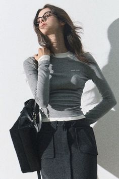 Woman with long hair and glasses wearing a gray long sleeve shirt and black pants