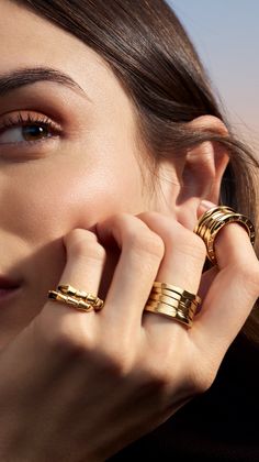 Close up of a woman's face and hand adorned with gold rings