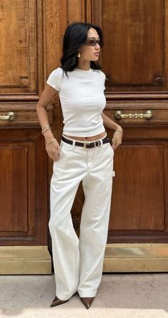 Woman in a white t-shirt and wide leg pants standing in front of a wooden door