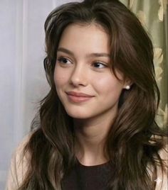 Young woman with long brown hair and pearl earrings looking to the side
