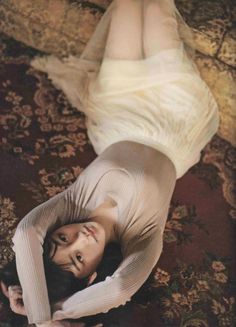 Woman with long dark hair lying on a patterned rug in a ribbed top and long skirt