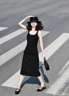 Woman in a black dress, hat, and glasses walking on a crosswalk