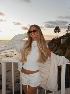 Woman with long blonde hair and sunglasses posing on a balcony at sunset