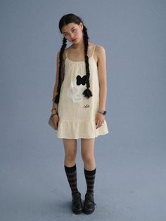 Woman with long braids wearing a cream dress with a skull print and plaid socks