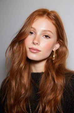 Woman with long red hair and freckles wearing a black sweater and gold earrings