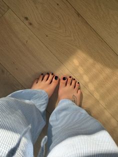 Bare feet with black nail polish on a light wood floor with striped pants