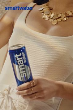Woman in a white tank top holding a Smartwater can, wearing a gold necklace