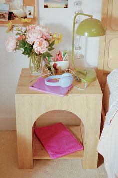 Nightstand with a vase of peonies, a green lamp, and electronics
