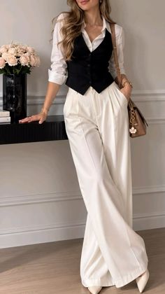 Woman in a white shirt, black vest, and white pants leaning on a table
