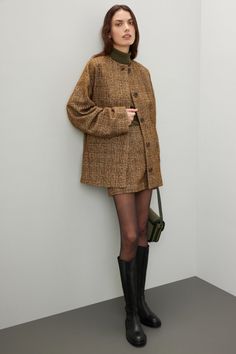 Woman in a plaid jacket and mini skirt with black boots and a green bag