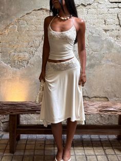 Woman in a white lace-trimmed dress and pearl necklace standing indoors
