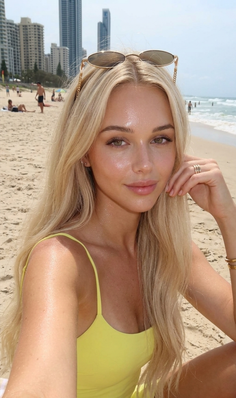 Blonde woman in a yellow swimsuit on a sunny beach with city buildings in background