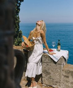 Woman in a white dress holding a basket of bread by the ocean