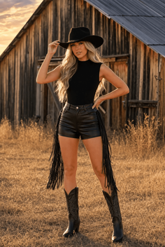 Woman in a cowboy hat and leather shorts posing in front of a barn at golden hour